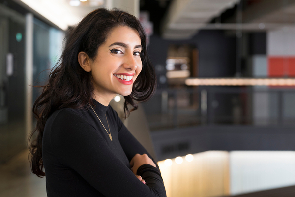 A person stands confidently, smiling at the camera, in a work environment.