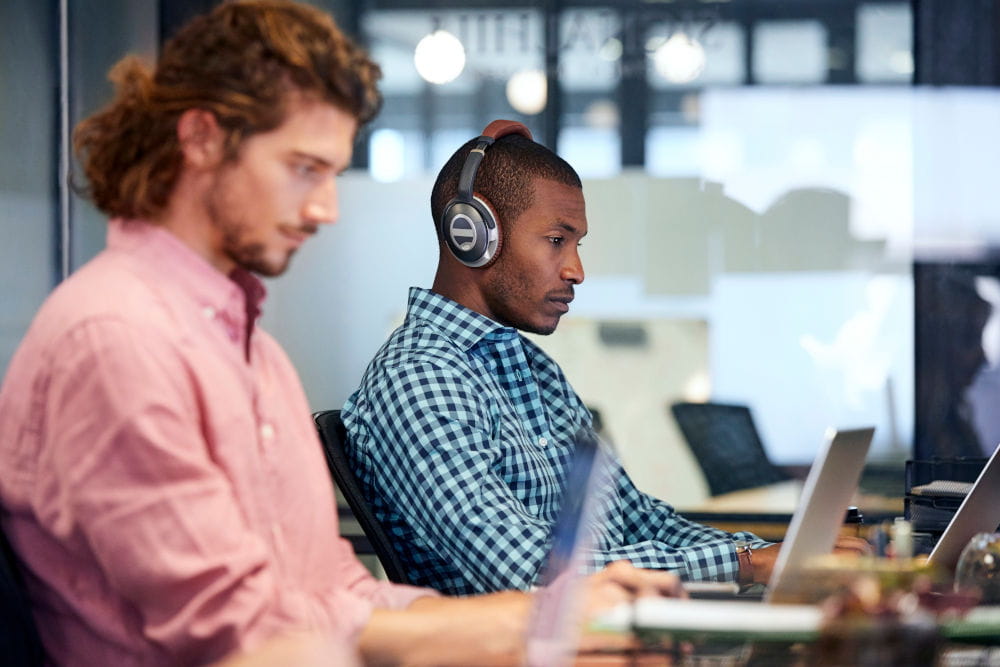 Two employees sitting at a table focused on their computer screens in a modern office environment.
