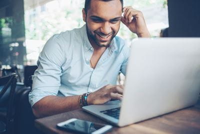 Un employé assis à une table, souriant tout en utilisant un ordinateur, affichant une attitude positive dans un environnement de travail.