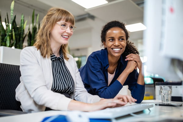 Twee werknemers aan een bureau, samen kijkend naar een computerscherm in een professionele werkomgeving.